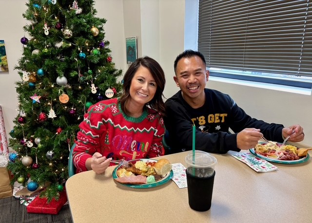 Two LBS employees eating and sitting beside each other in front of Christmas tree