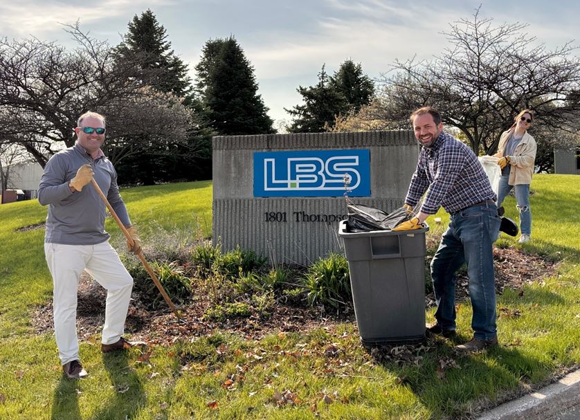Two LBS employees landscaping and smiling by LBS entrance sign